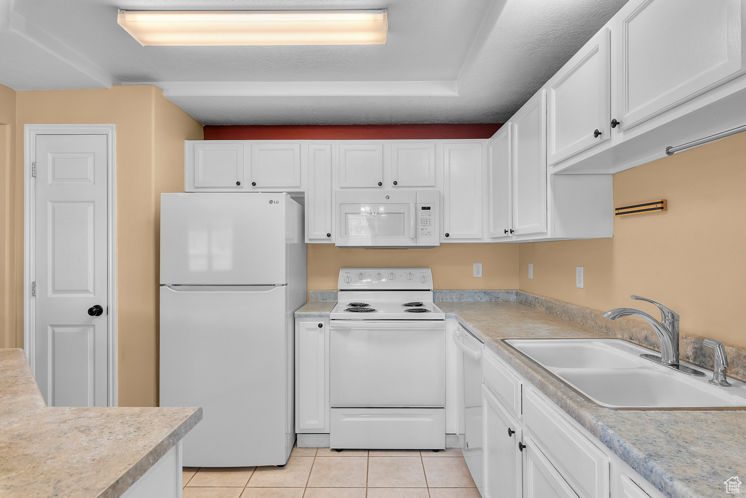 Kitchen featuring sink, white cabinets, white appliances, and light tile patterned floors