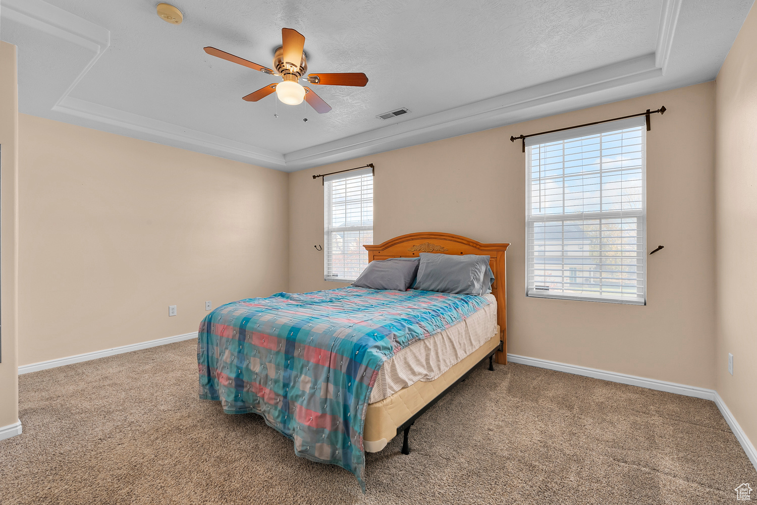 Bedroom with a raised ceiling, ceiling fan, carpet floors, and a textured ceiling