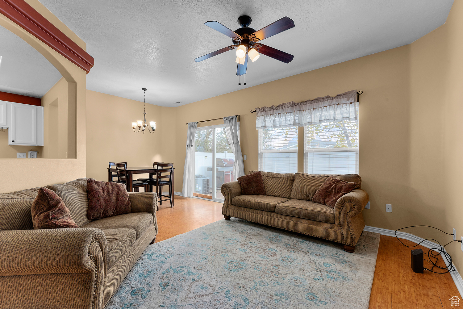 Living room with a textured ceiling, ceiling fan with notable chandelier, and light hardwood / wood-style flooring