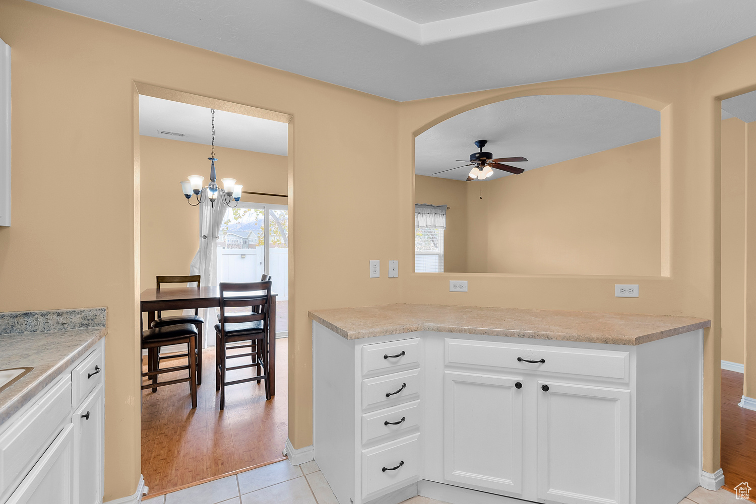 Kitchen with kitchen peninsula, light wood-type flooring, ceiling fan with notable chandelier, pendant lighting, and white cabinetry