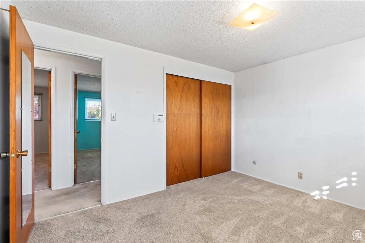 Unfurnished bedroom featuring a closet, light colored carpet, and a textured ceiling