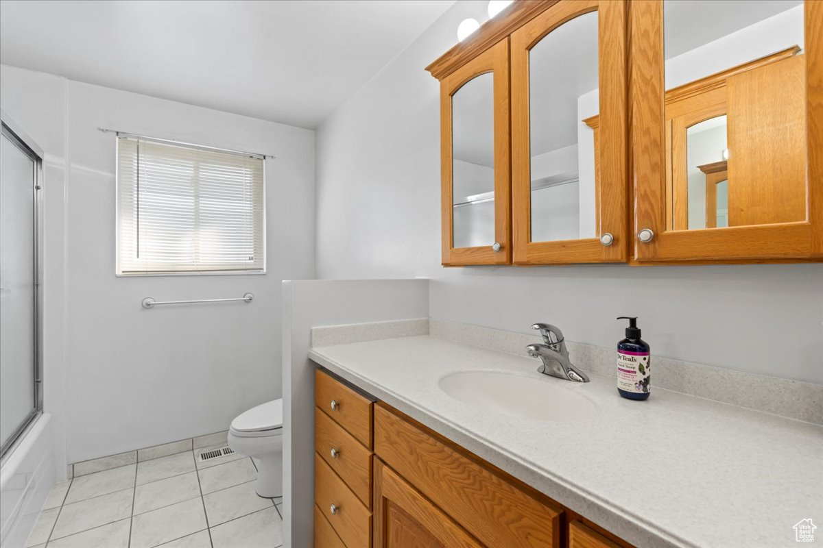 Full bathroom with tile patterned floors, vanity, toilet, and enclosed tub / shower combo