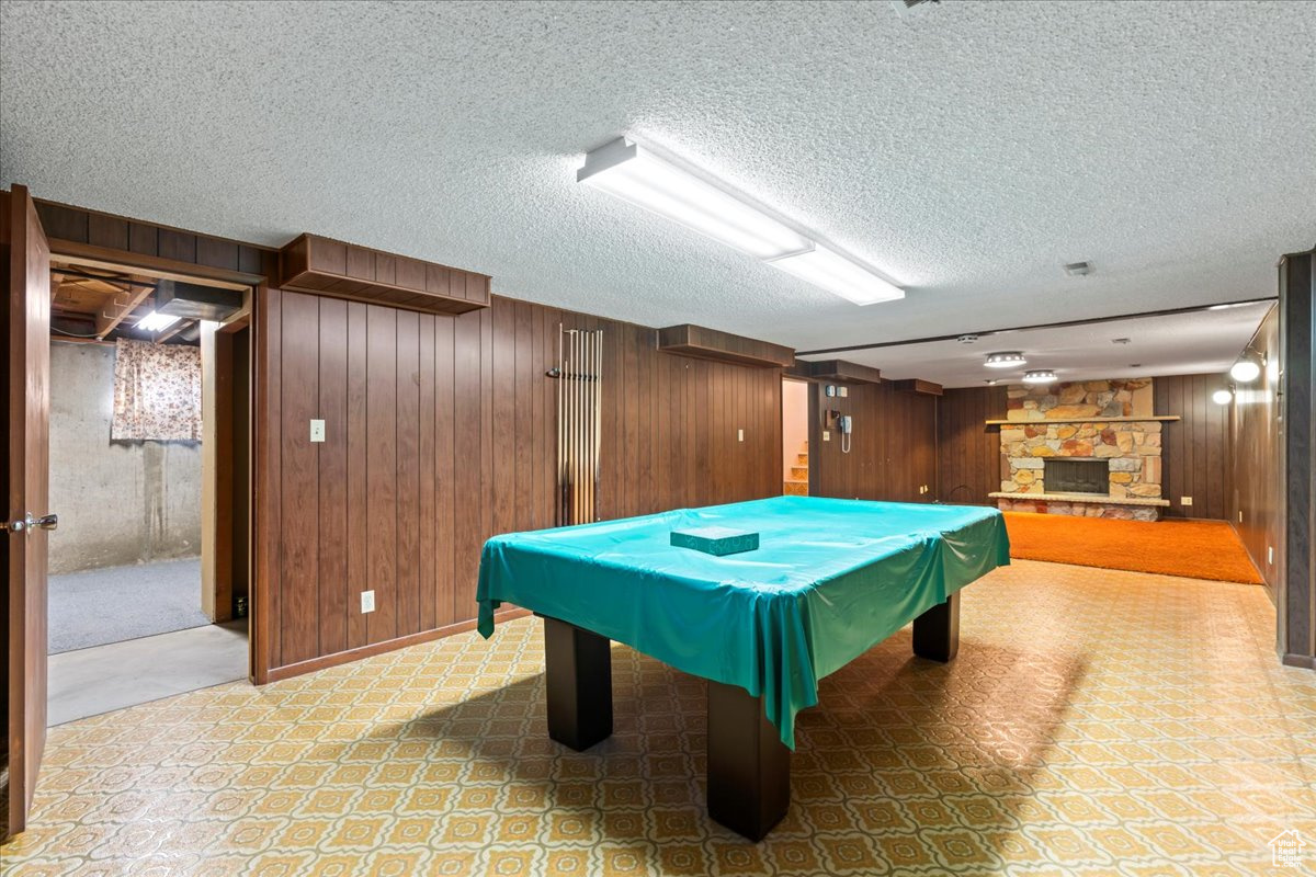 Recreation room with a fireplace, a textured ceiling, wooden walls, and billiards