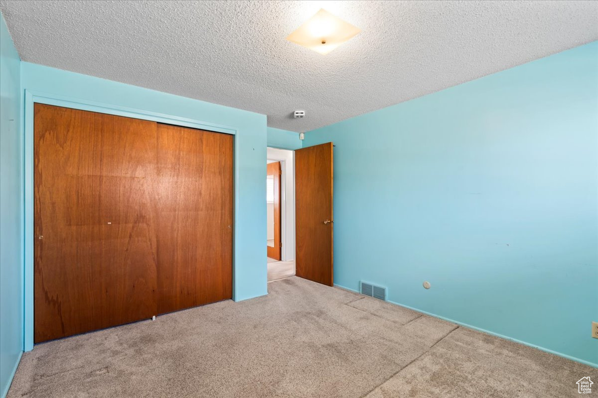 Unfurnished bedroom with a textured ceiling, carpet floors, and a closet