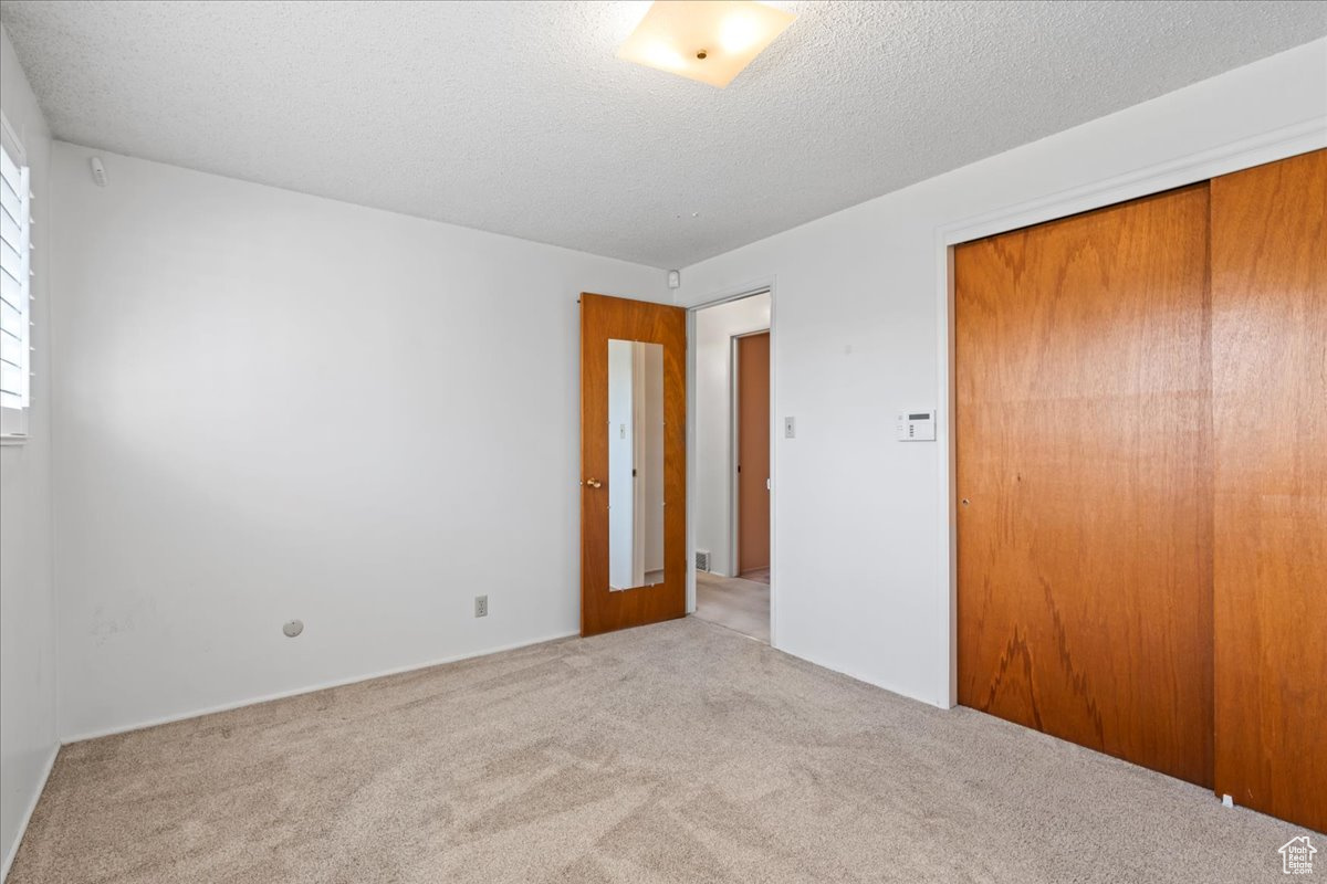 Unfurnished bedroom featuring a closet, light colored carpet, and a textured ceiling