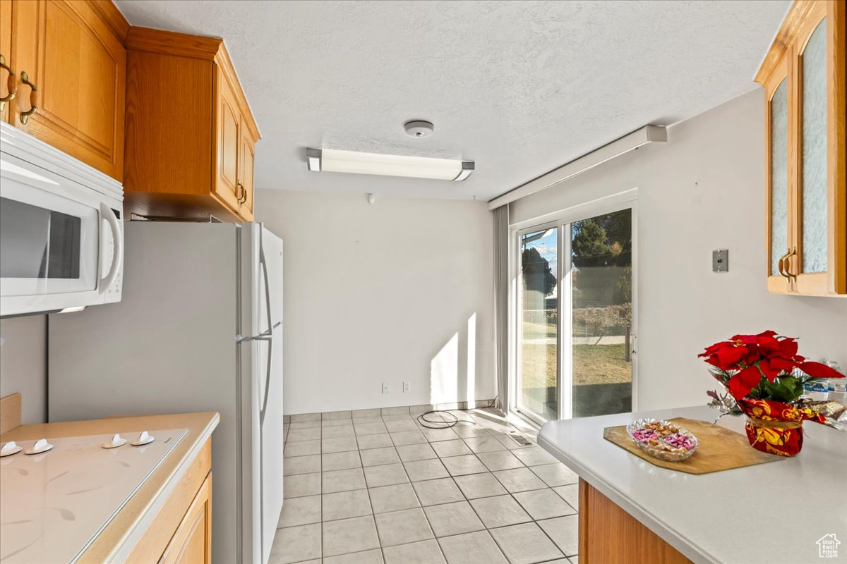 Kitchen with a textured ceiling, white appliances, and light tile patterned floors