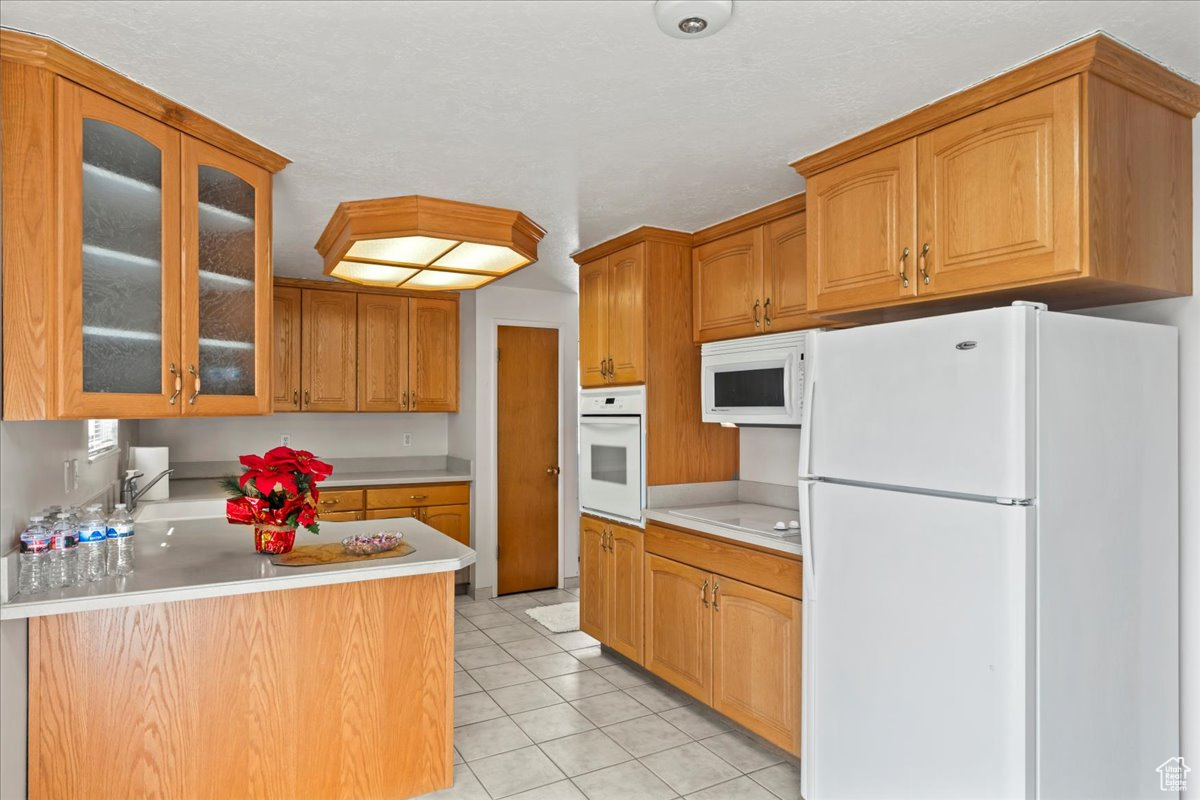 Kitchen with sink, white appliances, kitchen peninsula, and light tile patterned floors