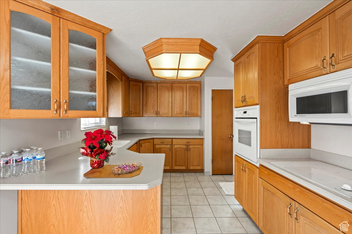 Kitchen with kitchen peninsula, light tile patterned floors, and white appliances