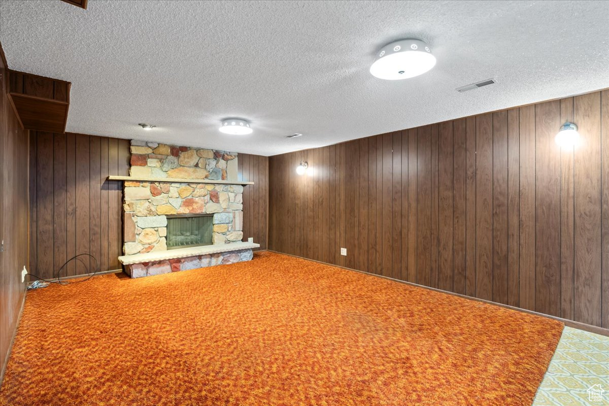 Basement featuring carpet flooring, a stone fireplace, a textured ceiling, and wooden walls