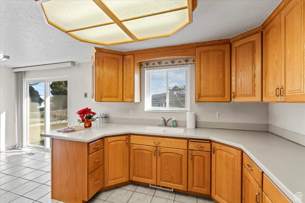 Kitchen with kitchen peninsula, sink, light tile patterned floors, and a textured ceiling