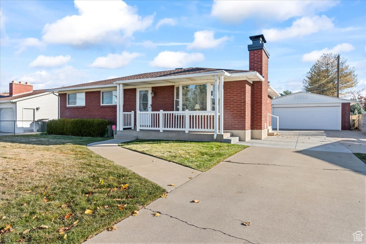 View of front of house with a porch, a front yard, an outdoor structure, and a garage