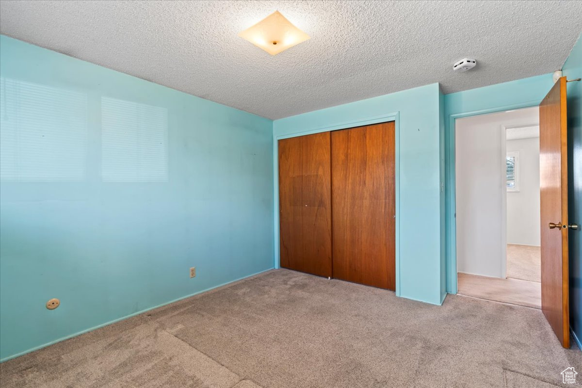 Unfurnished bedroom with light carpet, a textured ceiling, and a closet