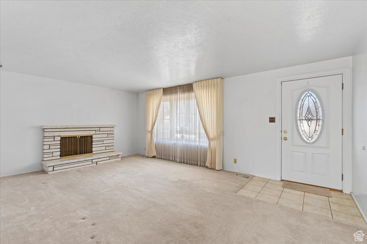 Entryway with light carpet, a fireplace, and a textured ceiling