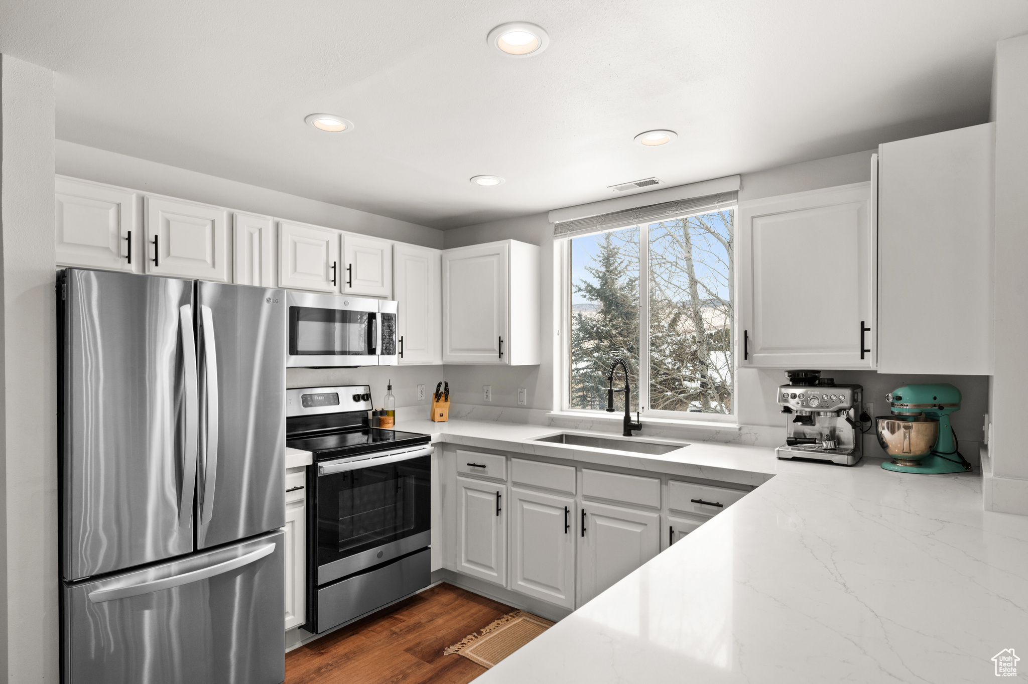 Kitchen featuring dark wood-type flooring, sink, light stone counters, white cabinetry, and stainless steel appliances