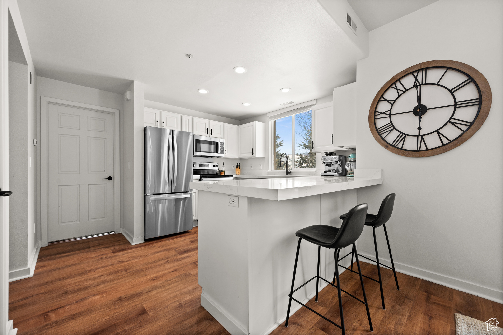 Kitchen featuring a kitchen breakfast bar, white cabinetry, dark hardwood / wood-style flooring, kitchen peninsula, and stainless steel appliances