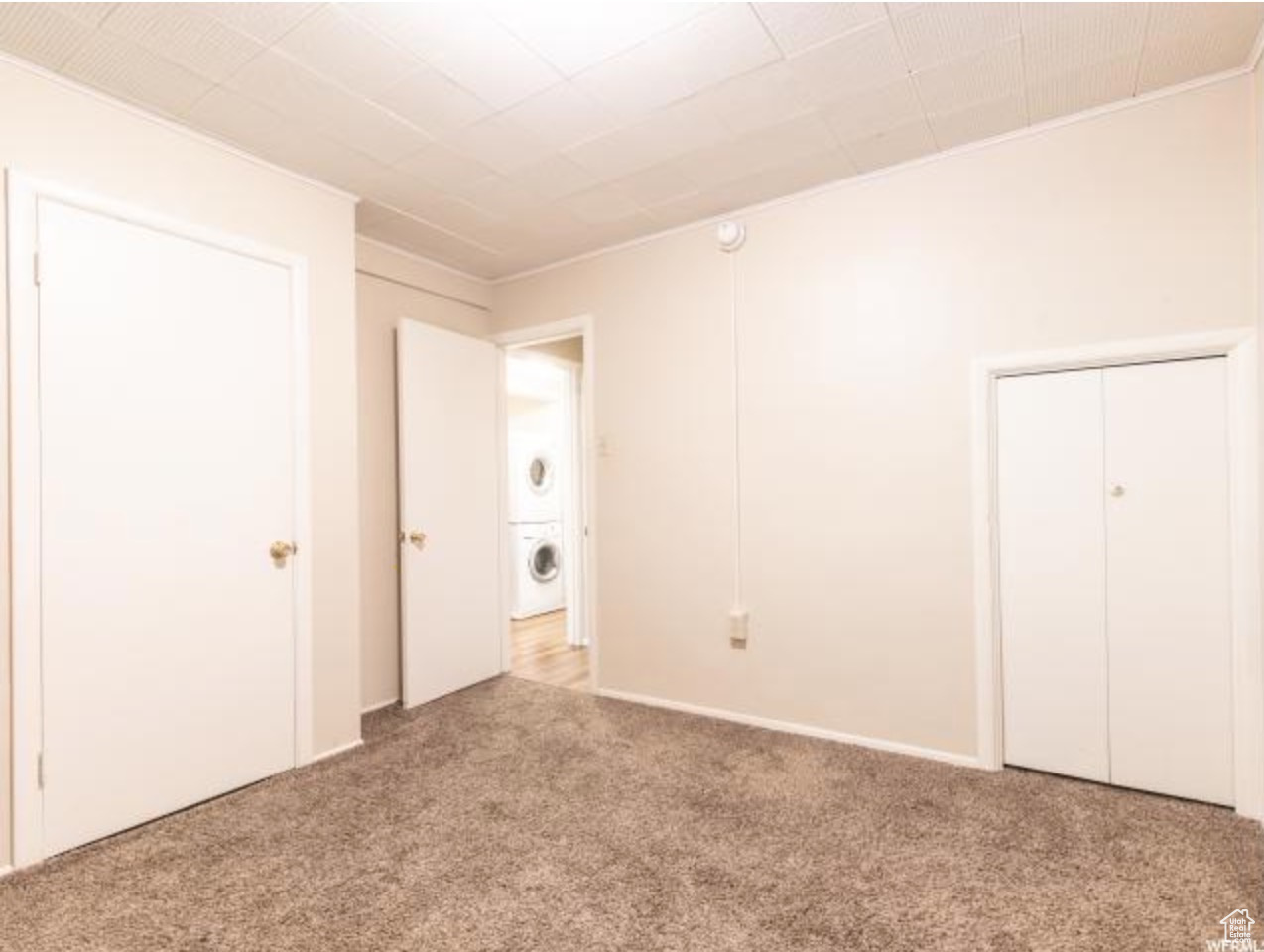 Unfurnished bedroom with light carpet and stacked washer and clothes dryer