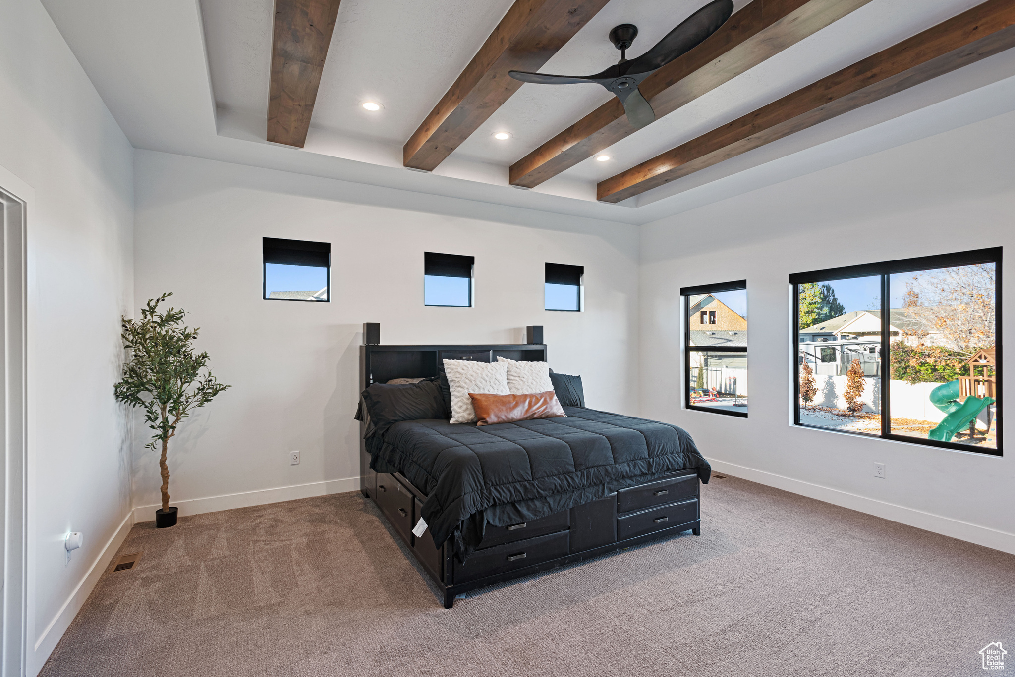 Carpeted bedroom with ceiling fan and beamed ceiling