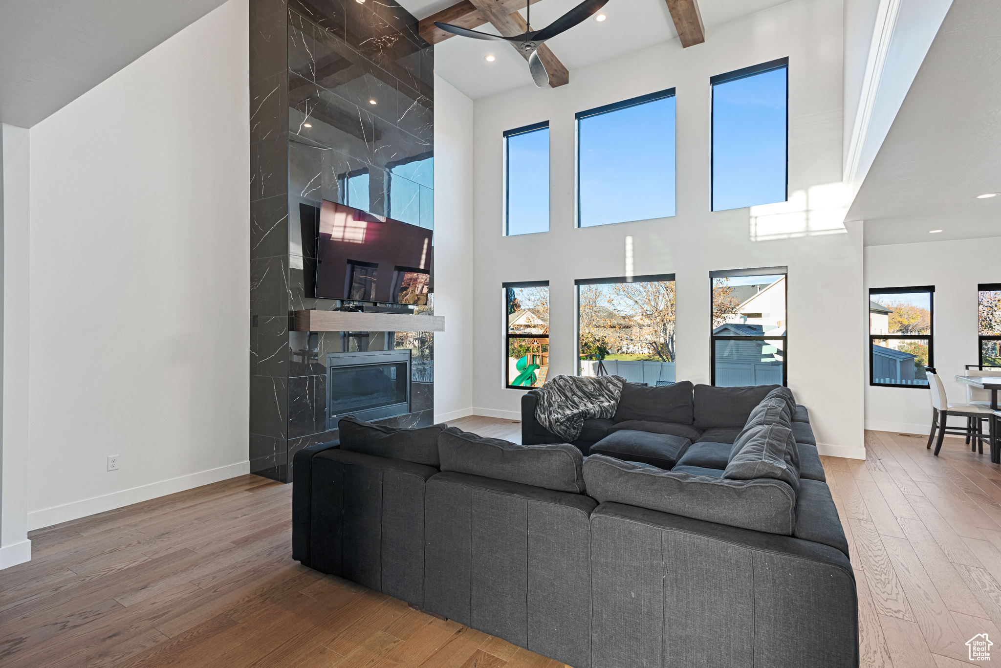 Living room with a high ceiling, ceiling fan, beamed ceiling, a fireplace, and hardwood / wood-style floors