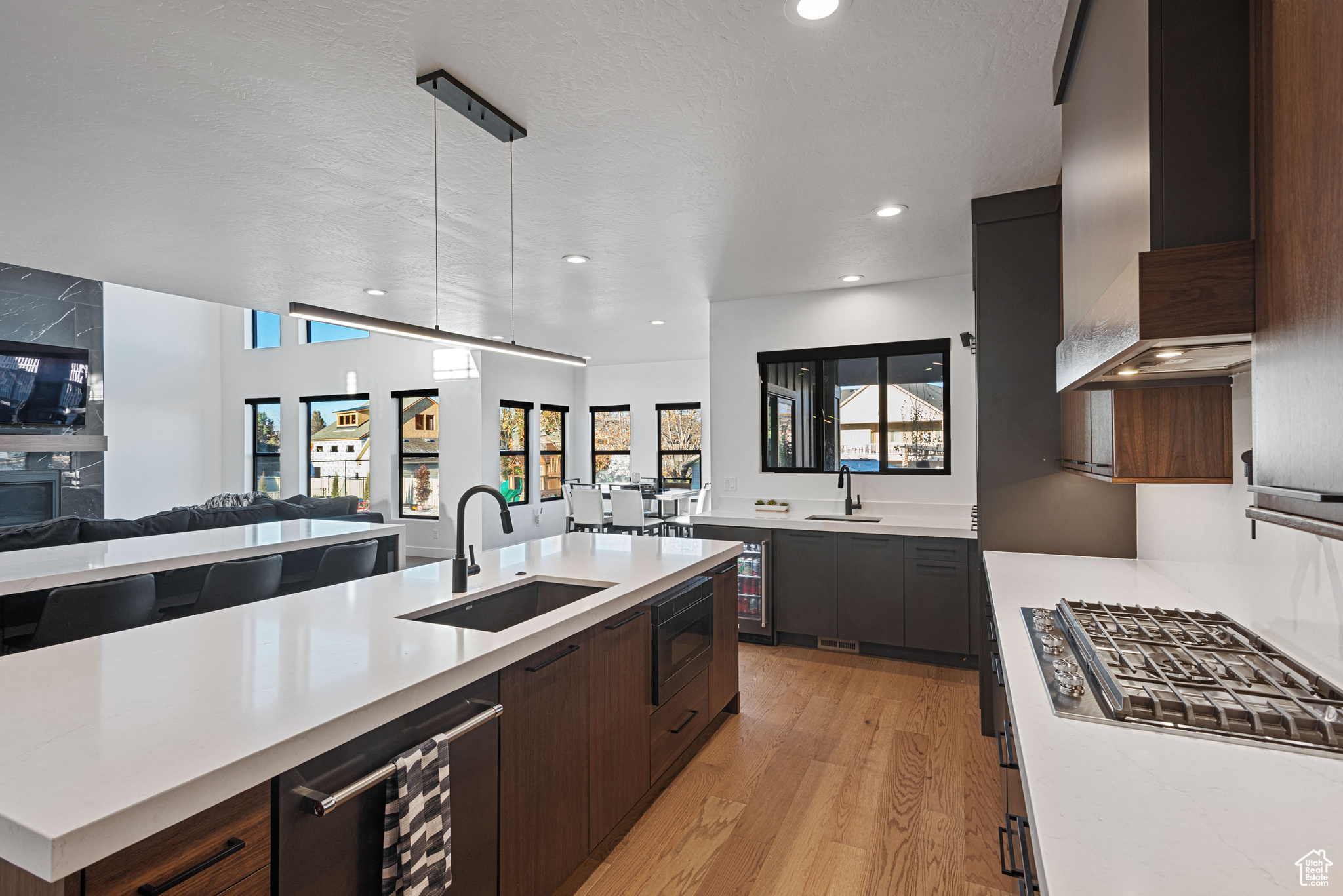 Kitchen featuring sink, hanging light fixtures, beverage cooler, wall chimney range hood, and light wood-type flooring