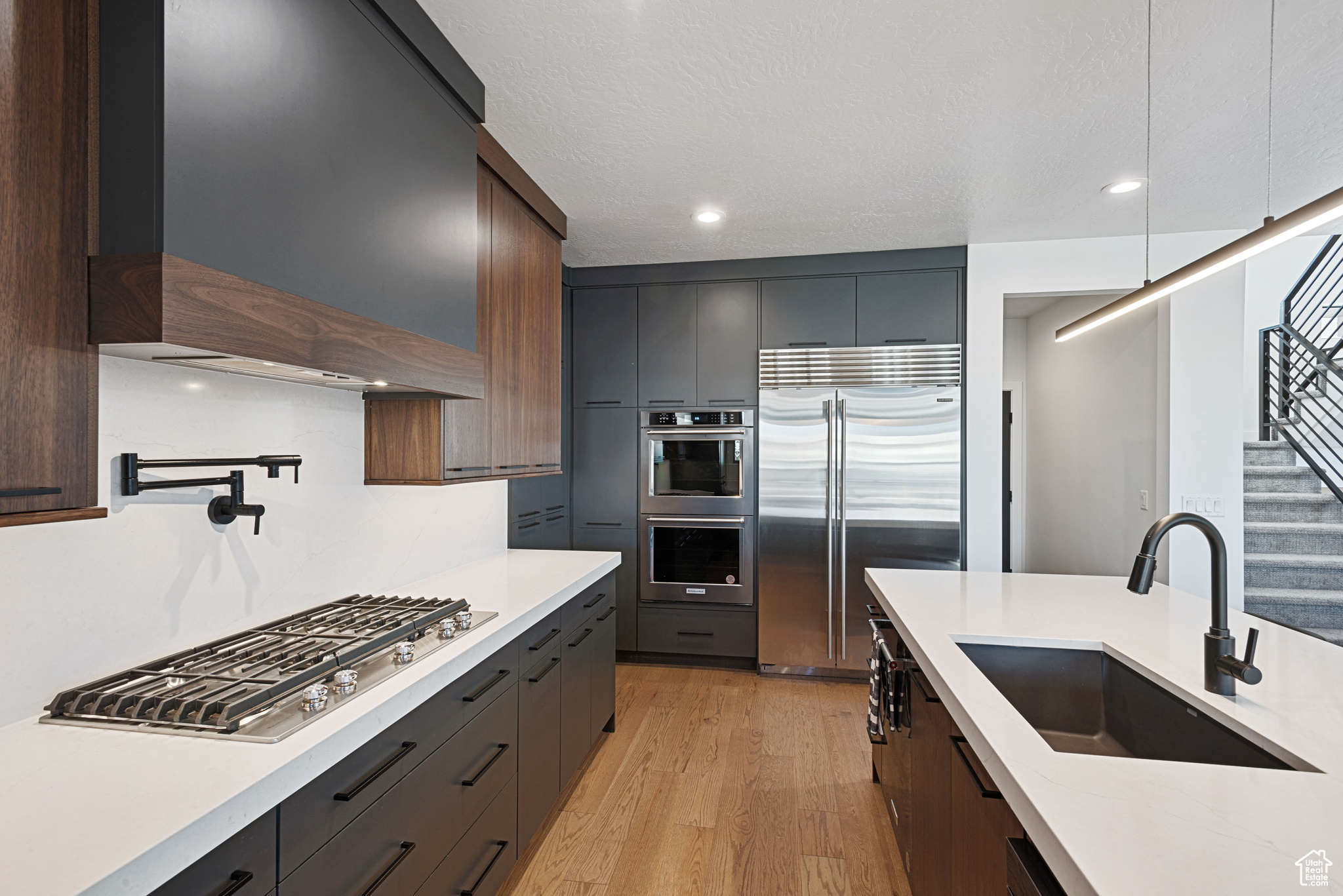 Kitchen with light wood-type flooring, custom range hood, dark brown cabinets, stainless steel appliances, and sink