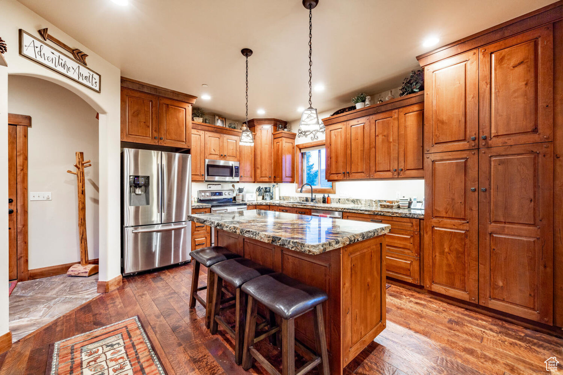 Kitchen with stainless steel appliances, a kitchen island, dark wood-type flooring, and light stone counters