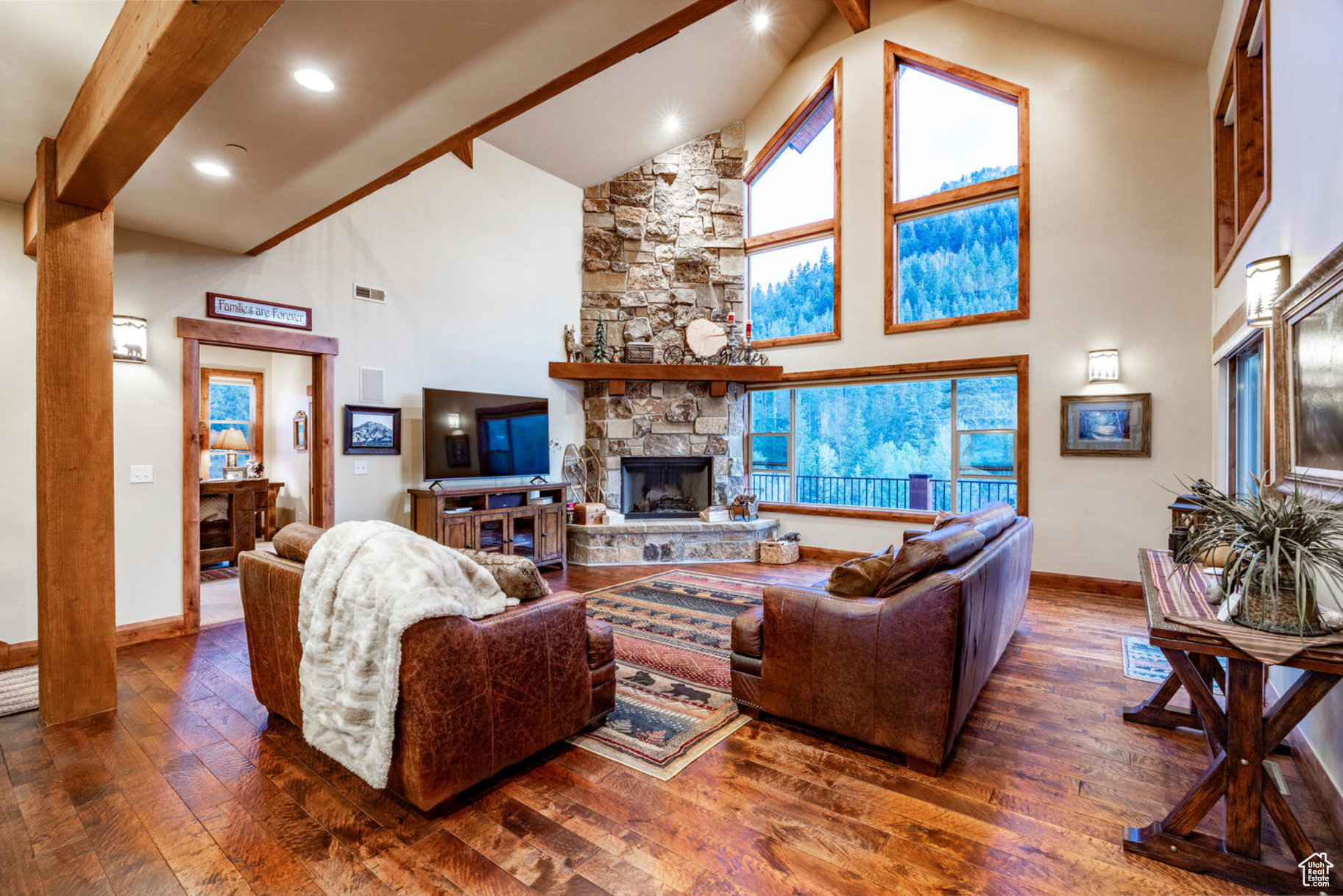 Living room featuring dark hardwood / wood-style floors, beam ceiling, a stone fireplace, and high vaulted ceiling