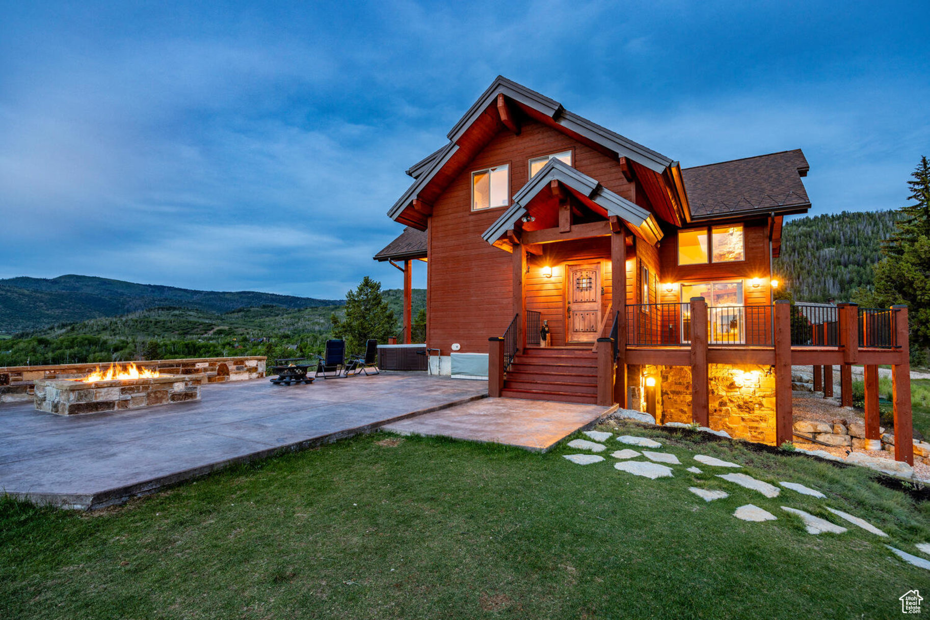 Back house at dusk featuring a patio area, a deck with mountain view, an outdoor fire pit, and a yard