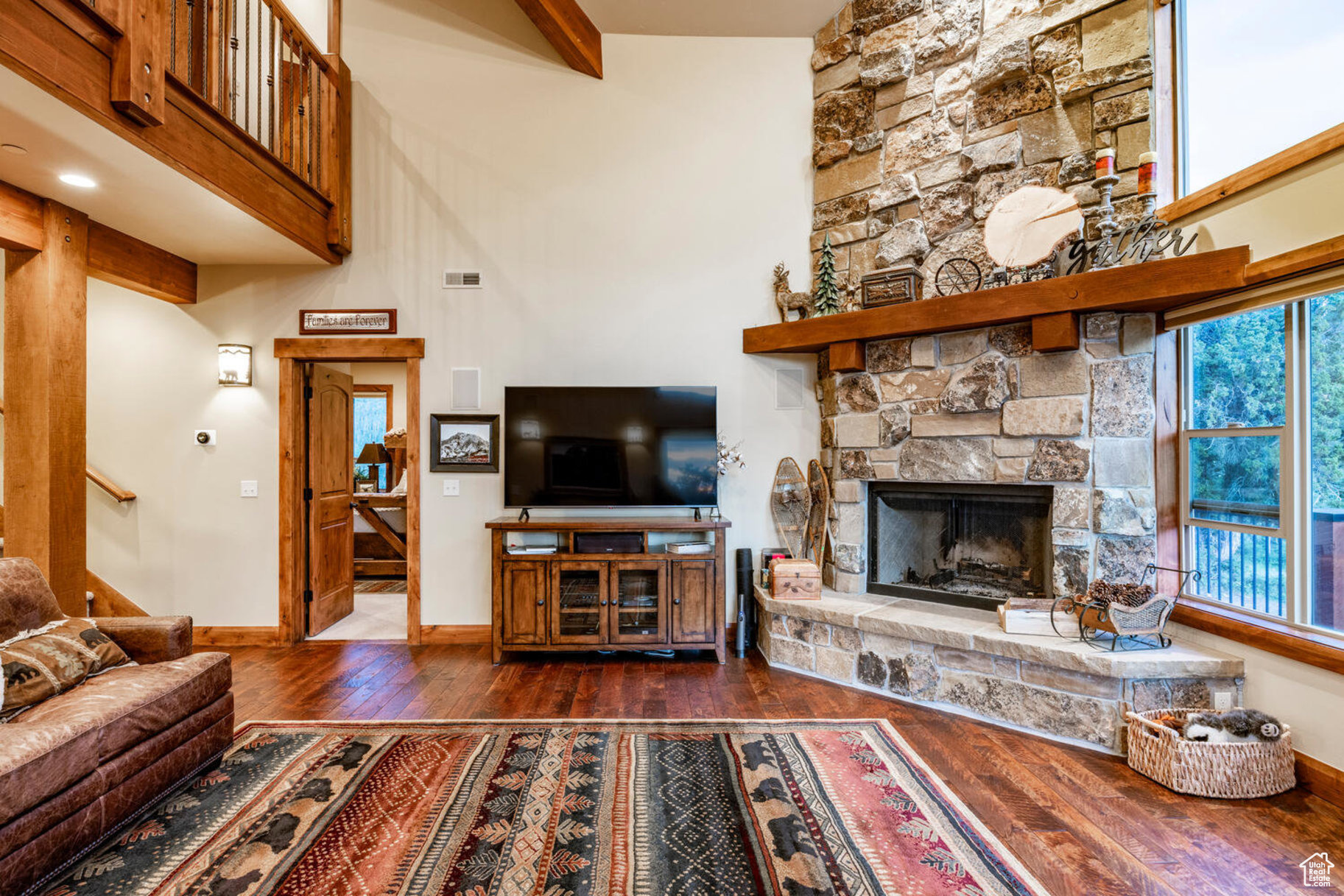 Living room with a stone fireplace, dark hardwood / wood-style flooring, and beam ceiling