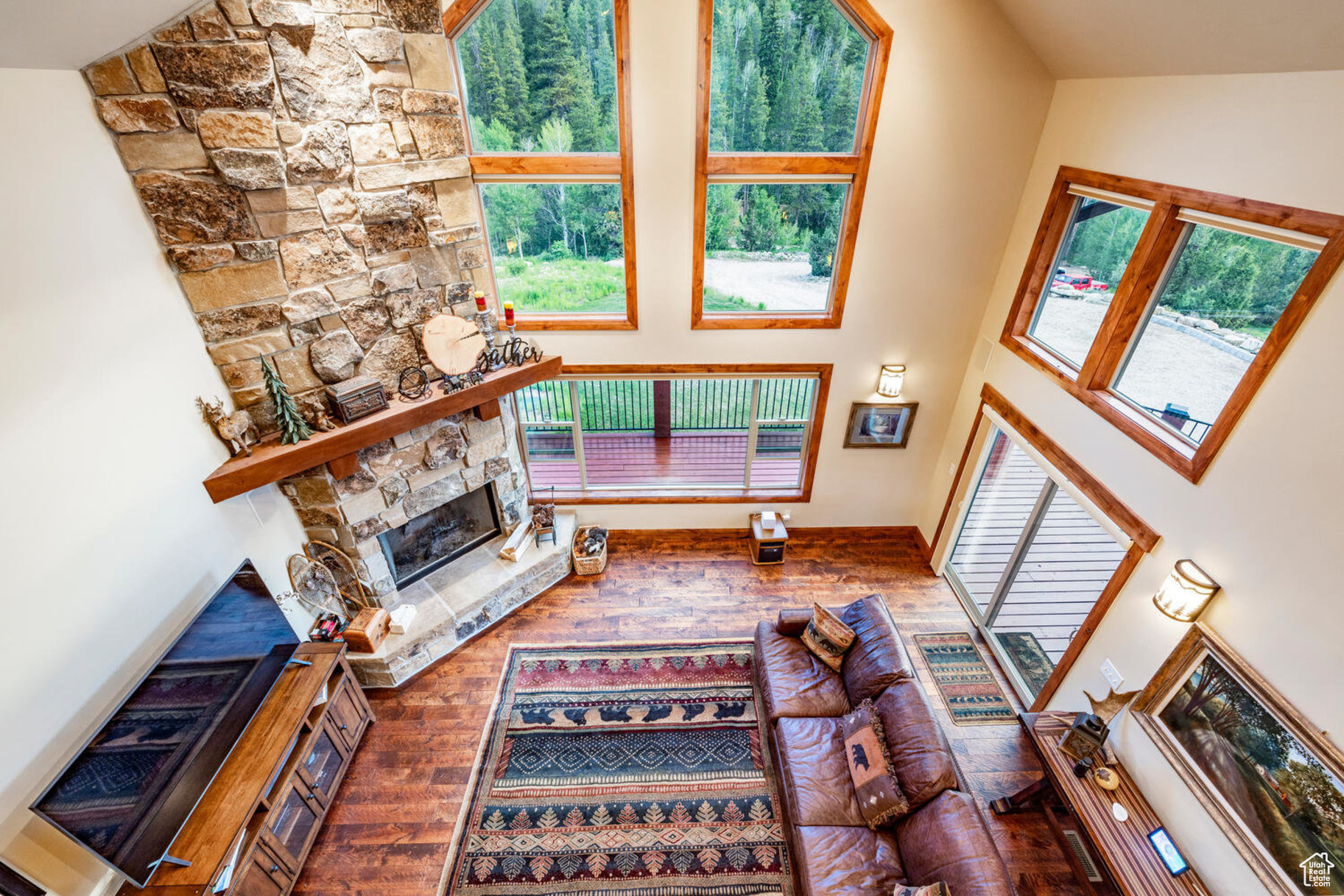 Living room featuring hardwood / wood-style floors, high vaulted ceiling, and a stone fireplace