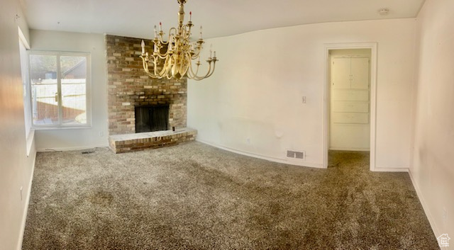 Unfurnished living room featuring a notable chandelier, carpet floors, and a brick fireplace