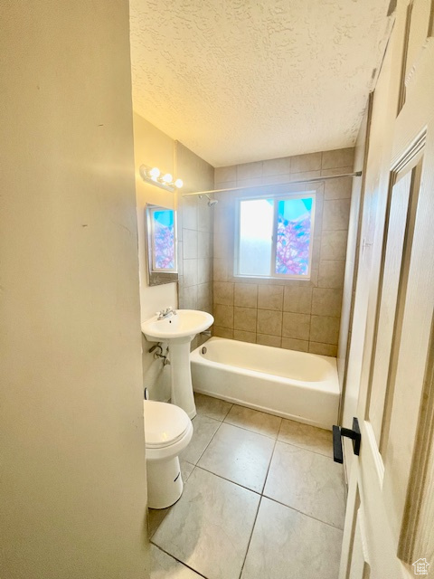 Bathroom with toilet, tile patterned flooring, a textured ceiling, and tiled shower / bath