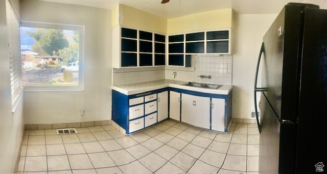 Kitchen with tasteful backsplash, black fridge, ceiling fan, light tile patterned floors, and white cabinetry