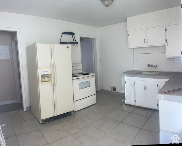 Kitchen with backsplash, light tile patterned floors, white cabinets, and white appliances