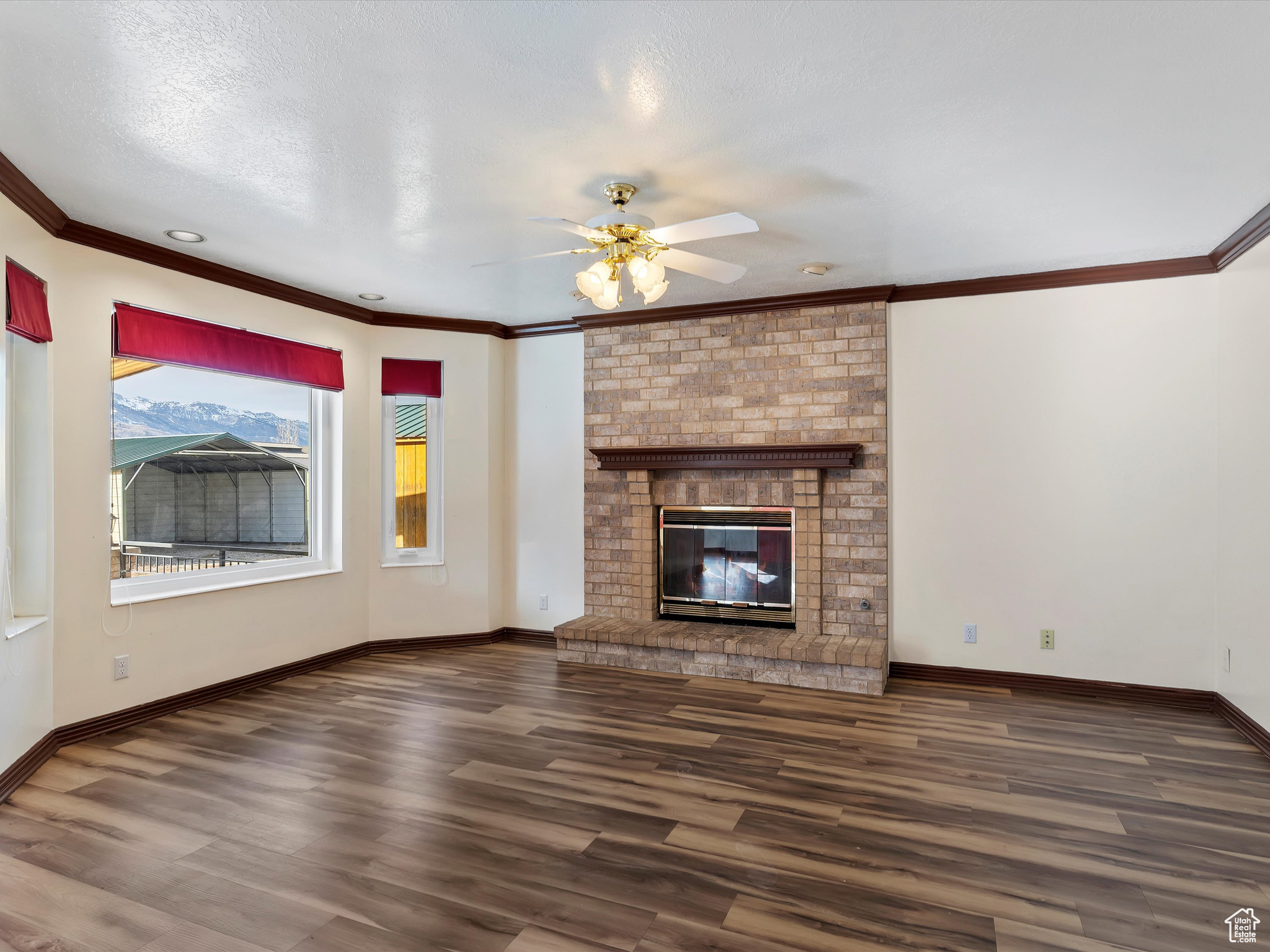 Unfurnished living room with ceiling fan, dark hardwood / wood-style flooring, crown molding, a textured ceiling, and a fireplace