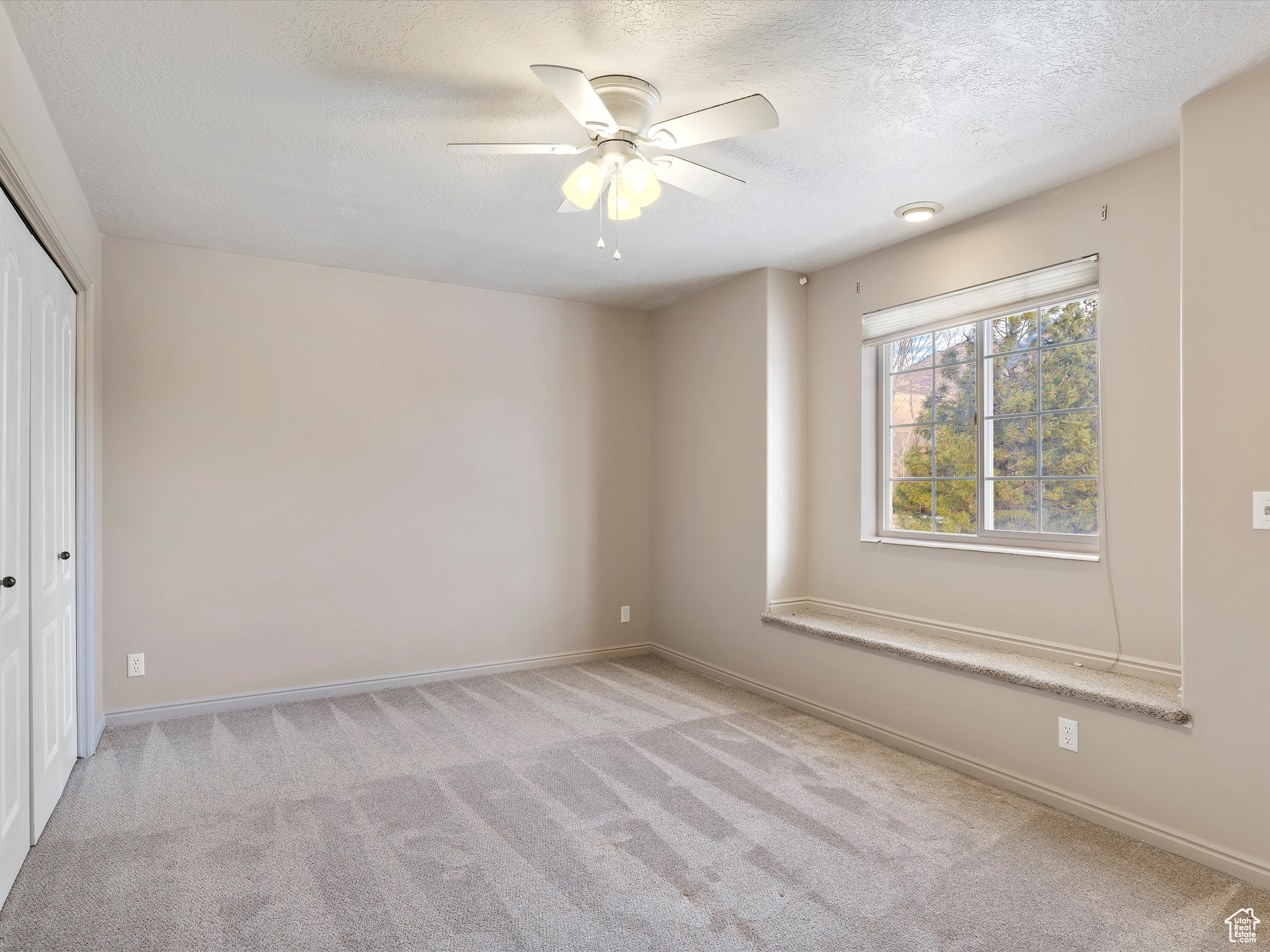 Empty room featuring ceiling fan, light colored carpet, and a textured ceiling