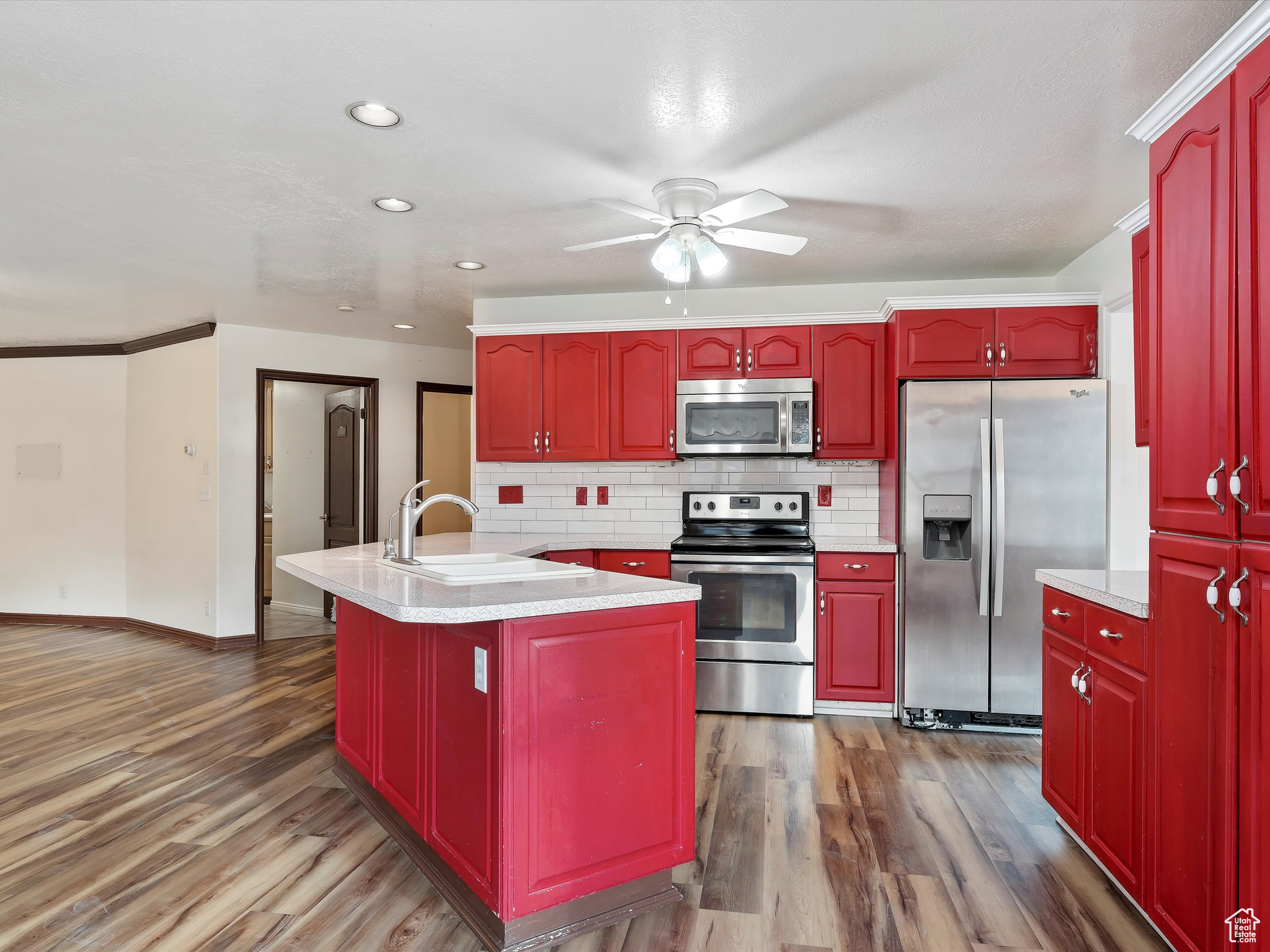 Kitchen with backsplash, a kitchen island with sink, dark wood-type flooring, sink, and appliances with stainless steel finishes