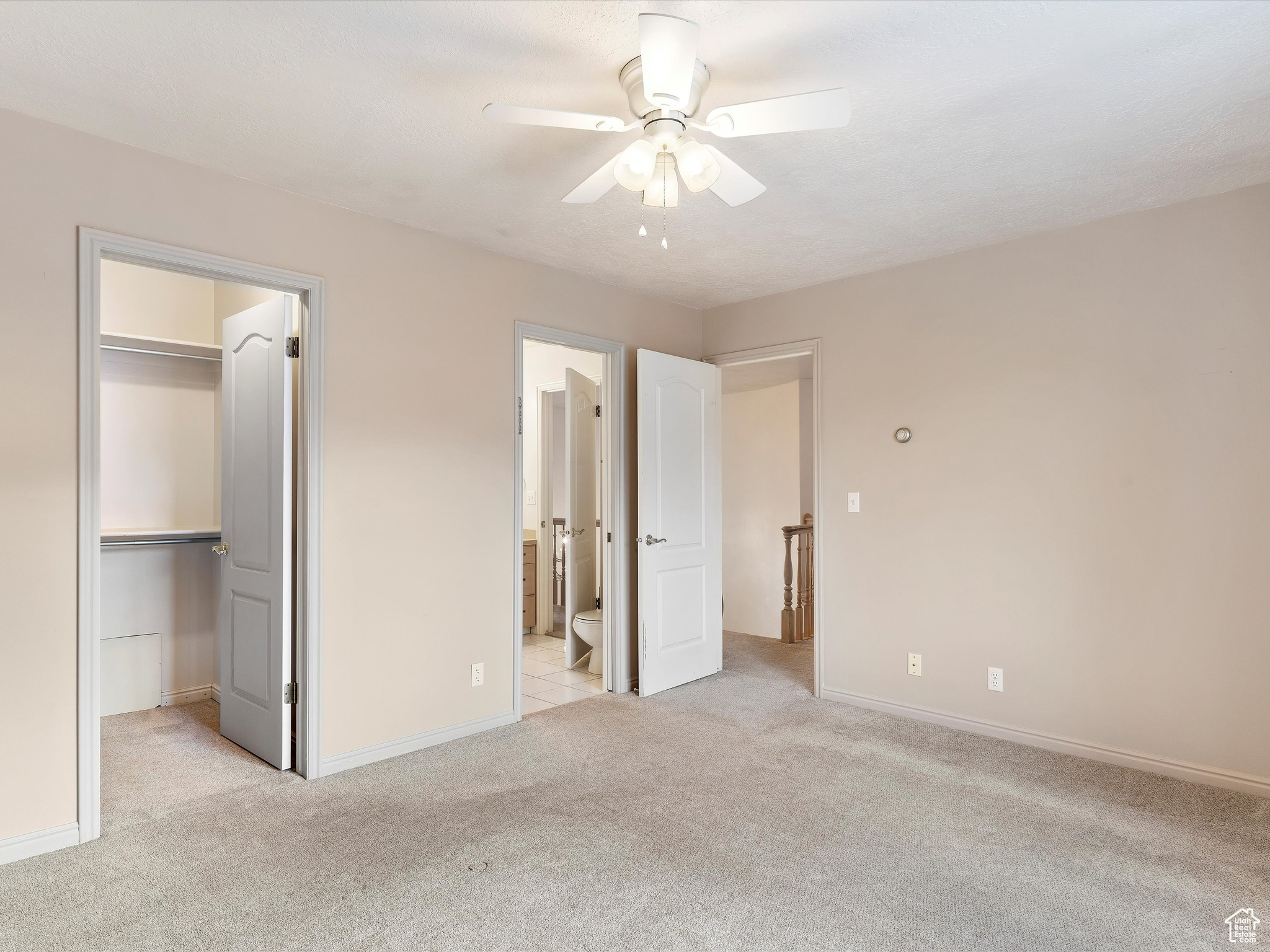 Unfurnished bedroom with light carpet, a walk in closet, ceiling fan, connected bathroom, and a closet