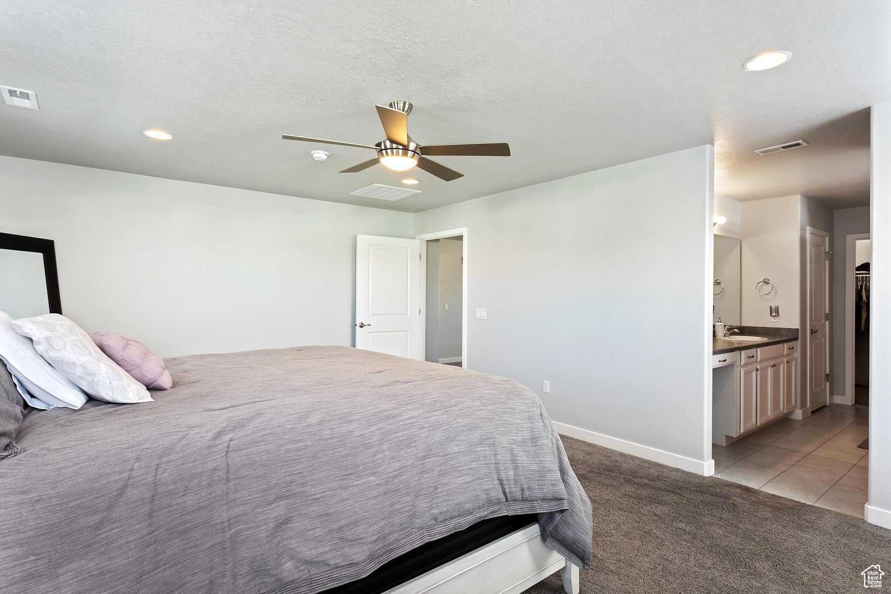 Bedroom featuring ceiling fan, sink, light carpet, and ensuite bath