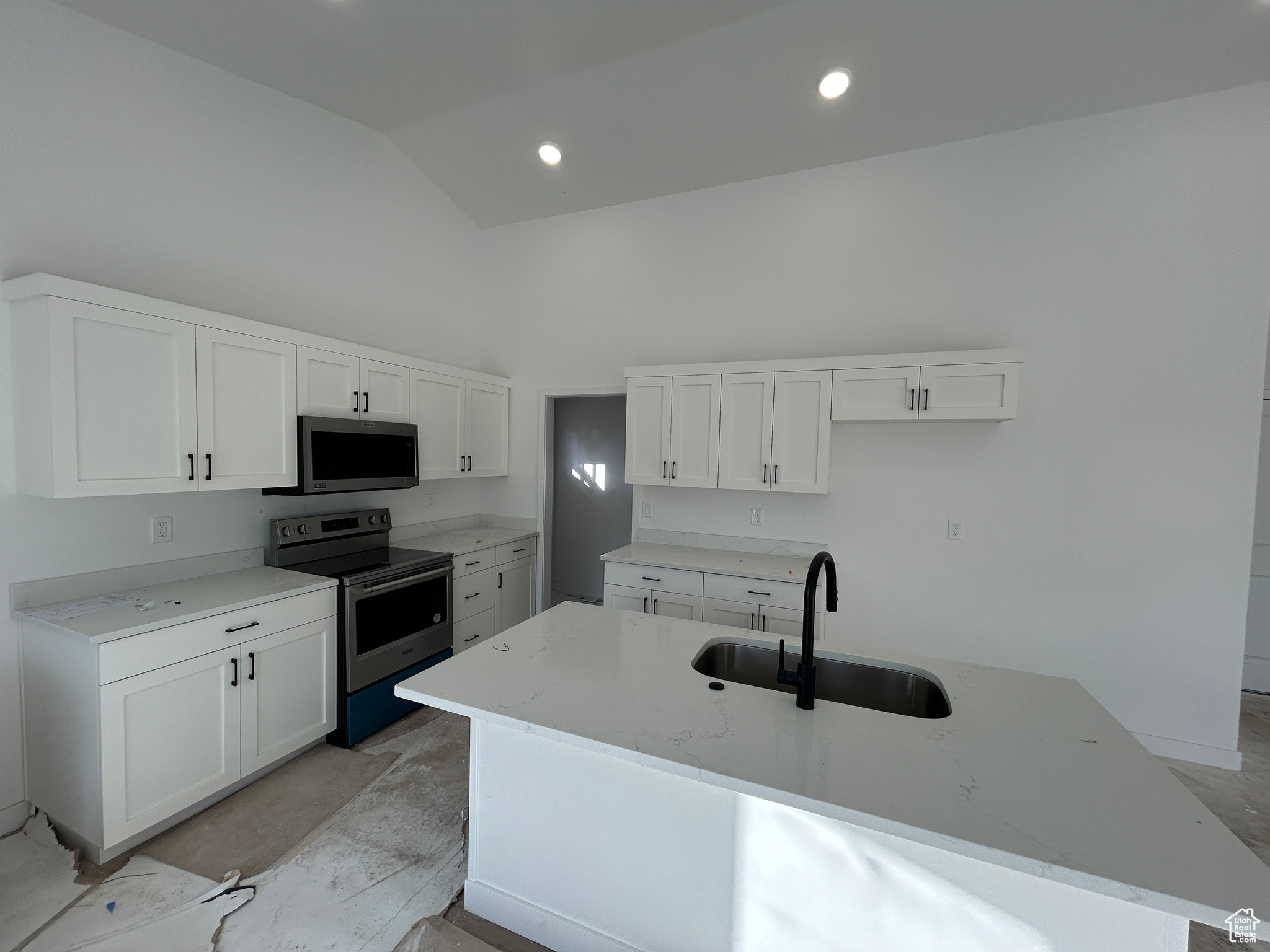 Kitchen with a kitchen island with sink, white cabinets, sink, light stone counters, and stainless steel appliances