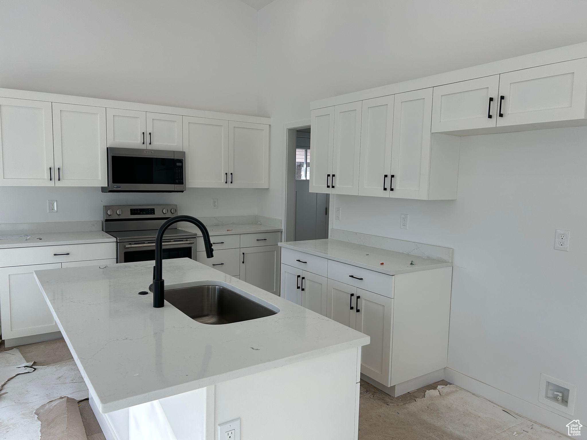 Kitchen featuring sink, stainless steel appliances, light stone counters, a center island with sink, and white cabinets