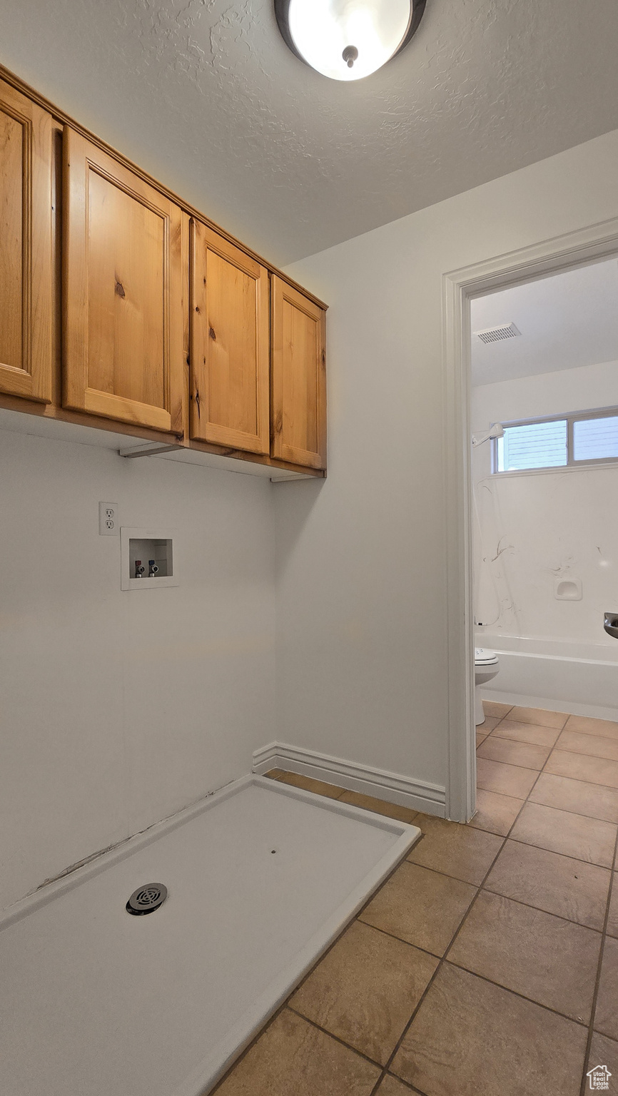 Laundry area with washer hookup, light tile patterned flooring, cabinets, and a textured ceiling