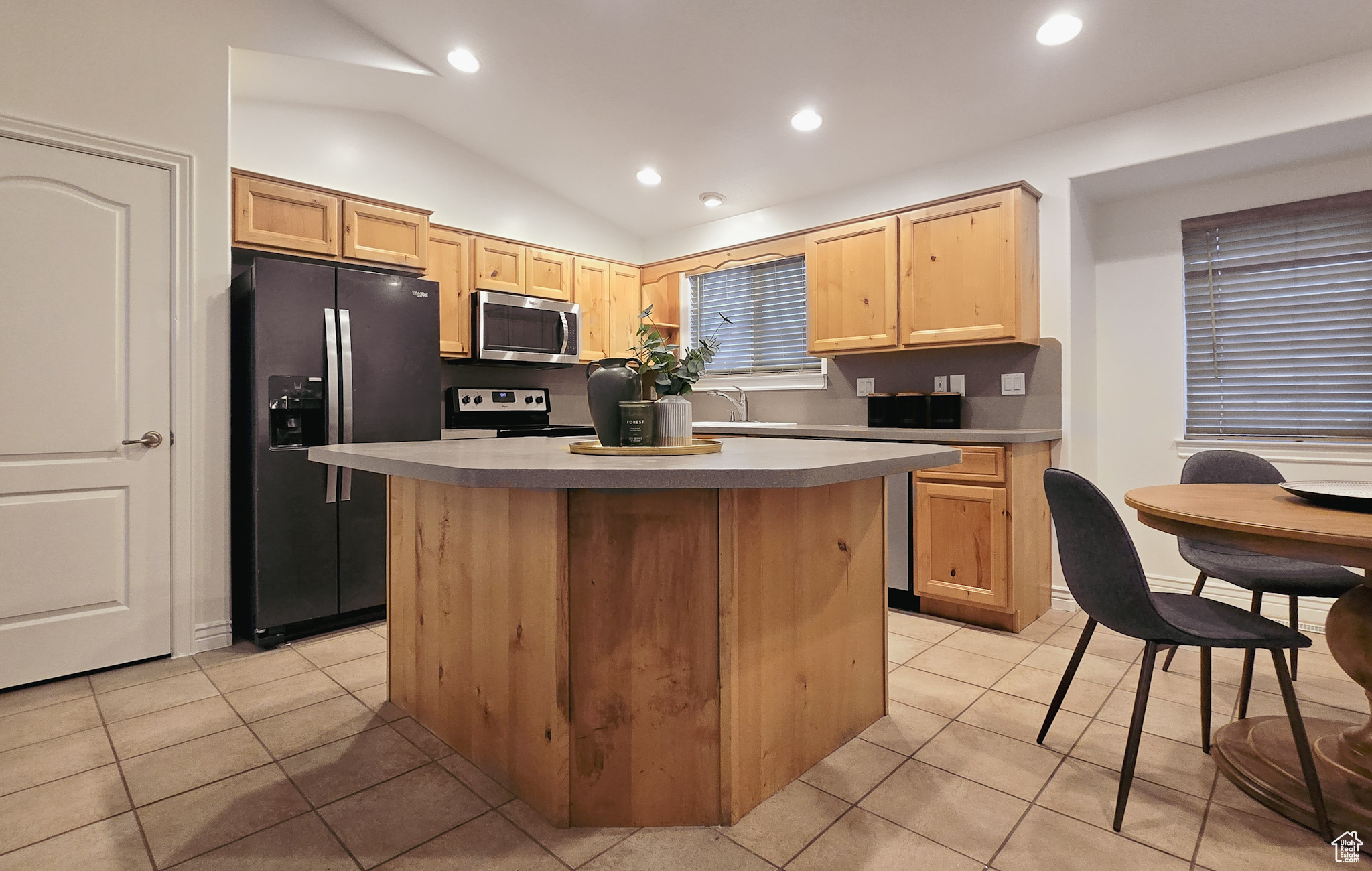 Kitchen featuring black refrigerator with ice dispenser, range with electric stovetop, lofted ceiling, light brown cabinetry, and a kitchen island