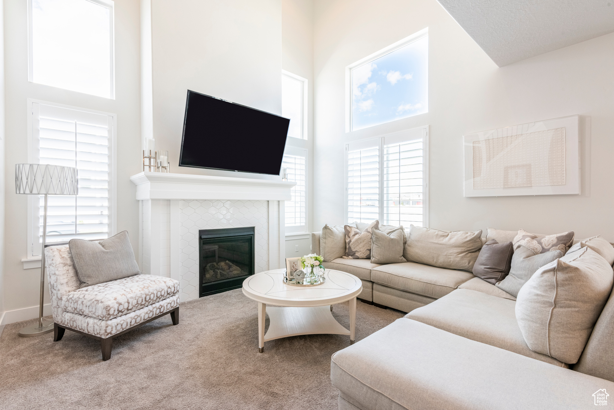 Carpeted living room with a tiled fireplace, a healthy amount of sunlight, and a high ceiling