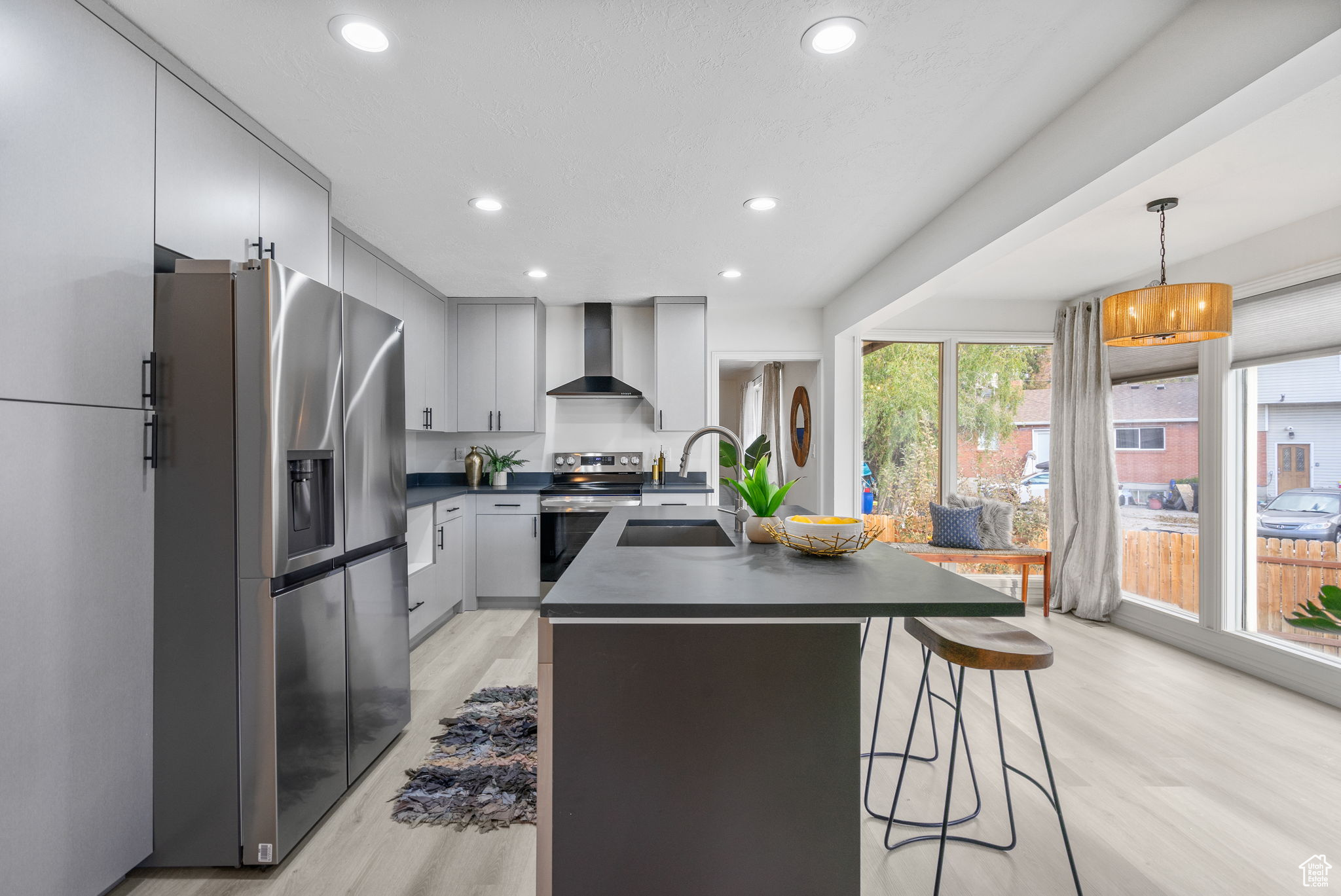 Kitchen with sink, wall chimney exhaust hood, hanging light fixtures, stainless steel appliances, and light wood-type flooring