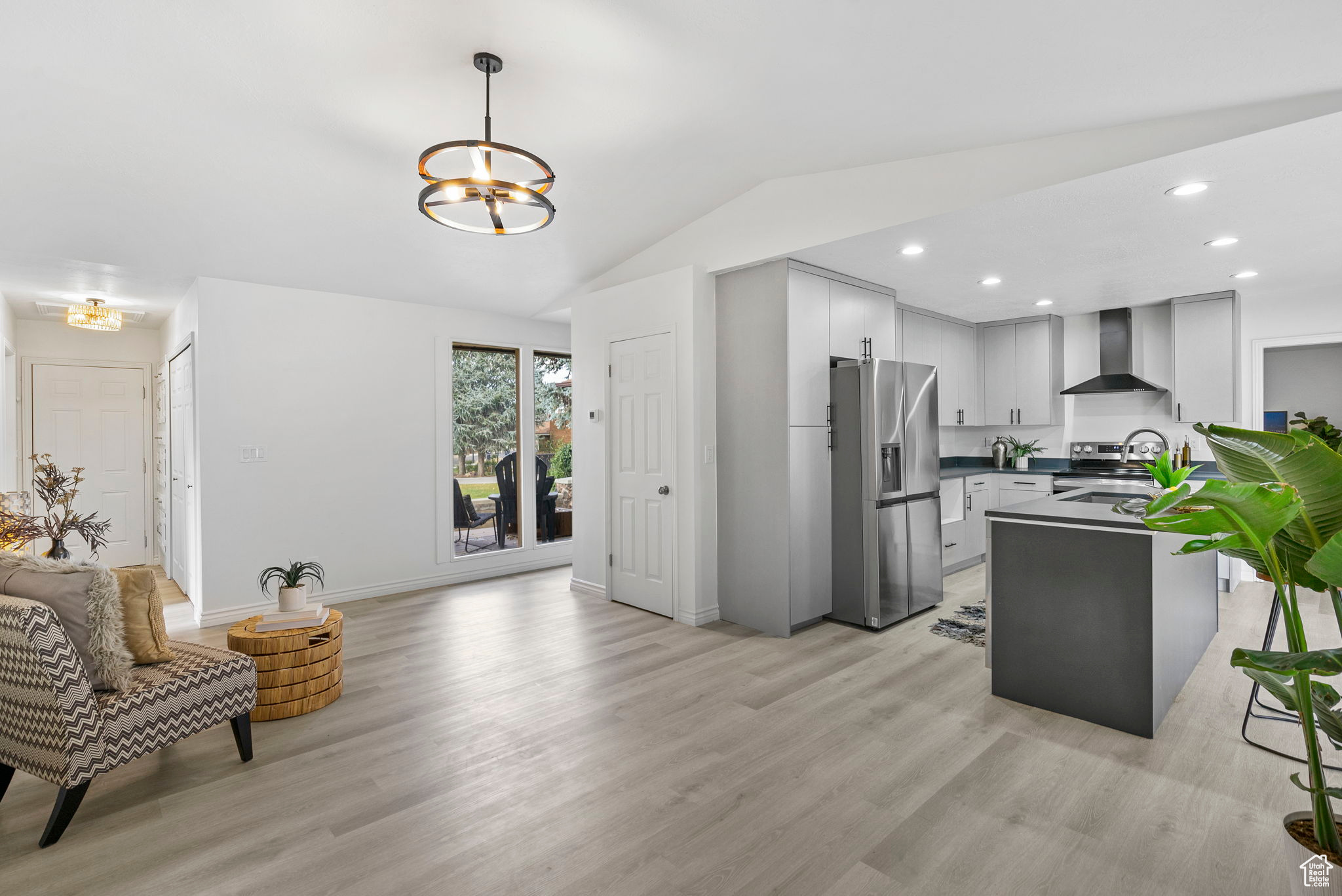 Kitchen with vaulted ceiling, wall chimney exhaust hood, light wood-type flooring, appliances with stainless steel finishes, and decorative light fixtures