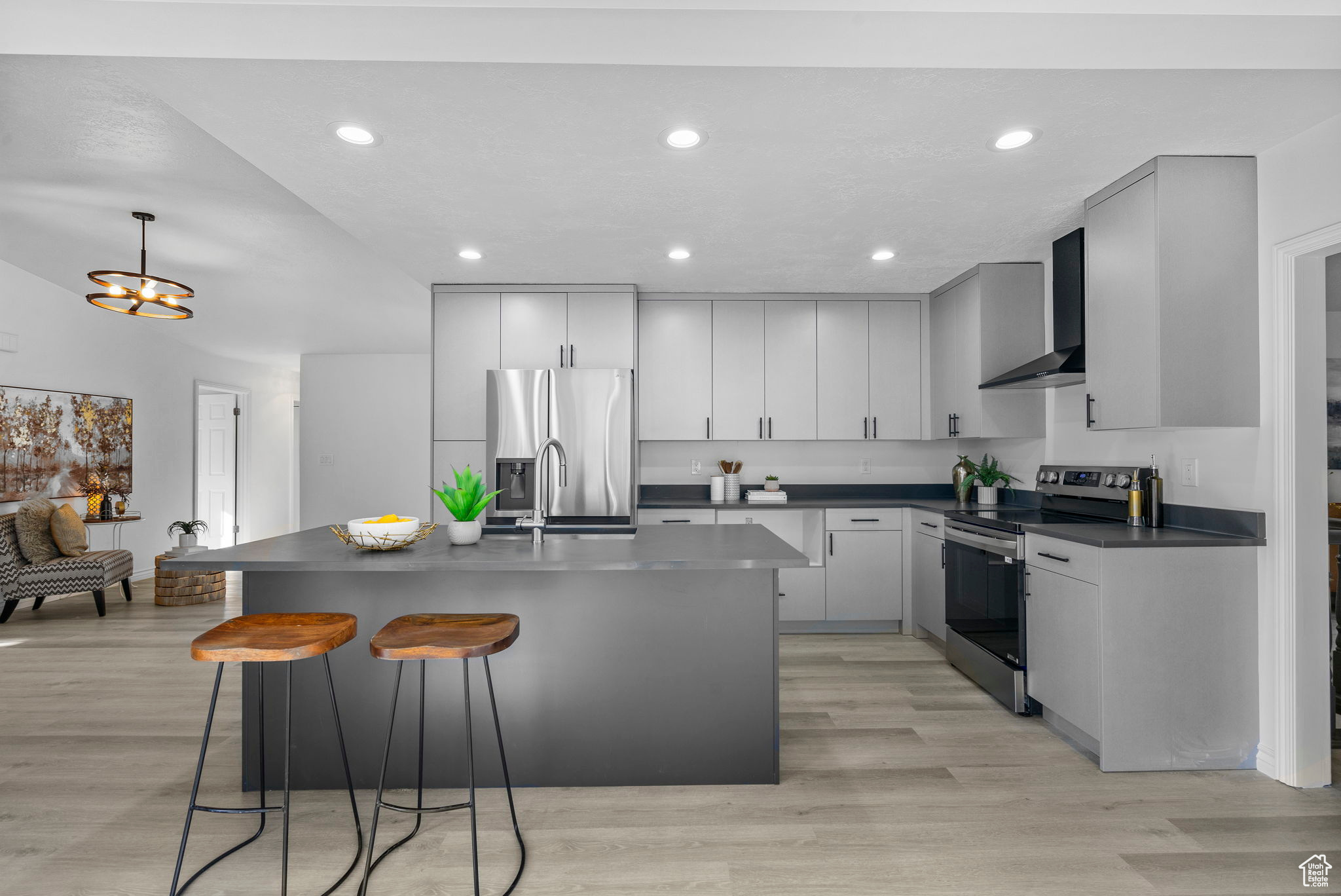 Kitchen featuring an inviting chandelier, wall chimney exhaust hood, light hardwood / wood-style floors, appliances with stainless steel finishes, and a kitchen island