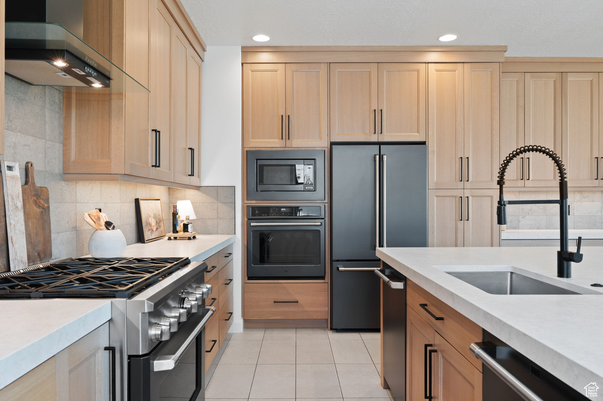 Kitchen featuring sink, light brown cabinets, premium appliances, light tile patterned floors, and exhaust hood