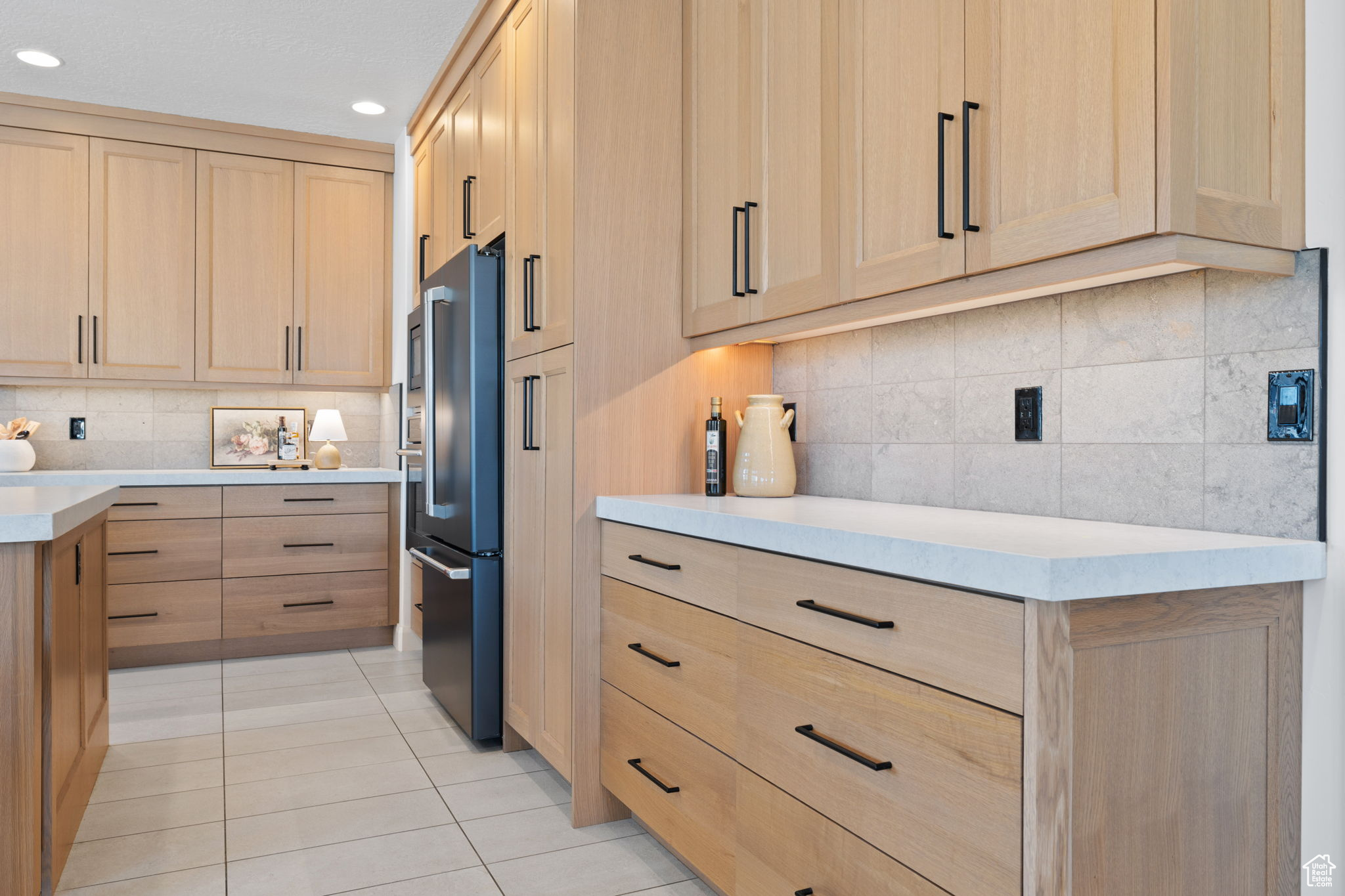 Kitchen featuring tasteful backsplash, stainless steel fridge, light brown cabinetry, and light tile patterned floors