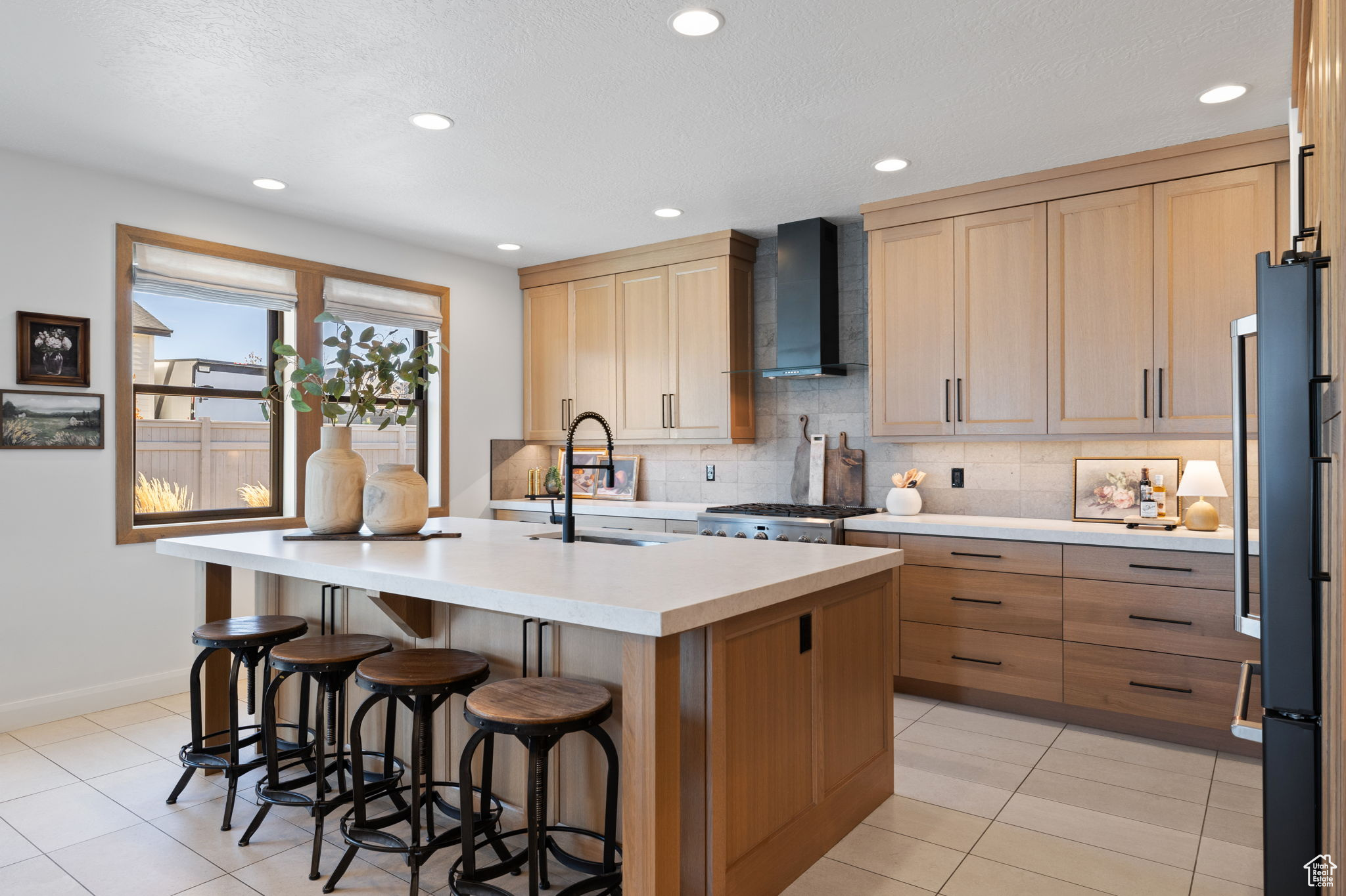 Kitchen with decorative backsplash, sink, wall chimney range hood, a center island with sink, and a breakfast bar area