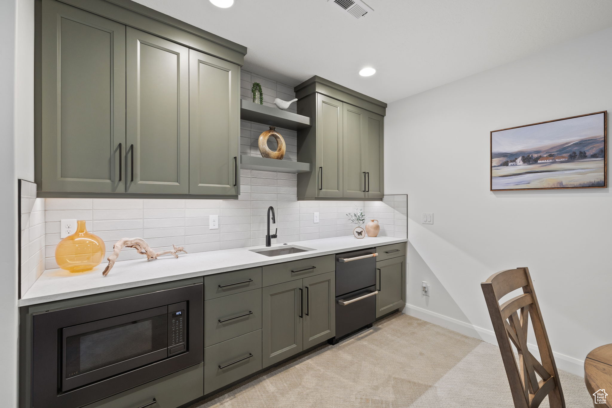 Kitchen with backsplash, light colored carpet, black microwave, sink, and green cabinets